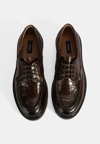 Braune Lederschuhe mit polierter Textur, ausgestattet mit Schnürdesign, runden Zehen und dünnen Gummisohlen. Markenlogo sichtbar im Inneren.