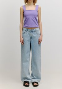 Paarse tanktop met vierkante hals, lichtblauwe wijd uitgesneden jeans, zwarte slide sandalen. Kenmerken zijn onder andere grote zakken en een ontspannen pasvorm.