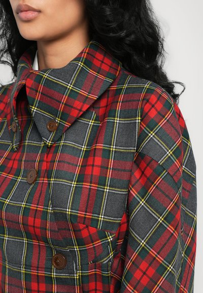 Giacca a quadri con ampio colletto, caratterizzata da un motivo tartan rosso, verde e giallo su sfondo grigio. Bottoni marroni visibili.