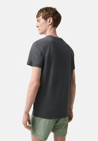 Mørkegrå bomulds t-shirt med korte ærmer, en rund halsudskæring og diskrete sideslids, parret med lysegrønne shorts.