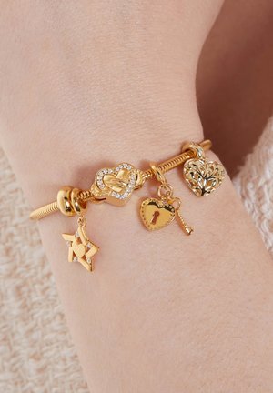 Gouden armband met verschillende bedels: een hart met kristallen, een ster, een sleutel en een blad, allemaal met gedetailleerde gravures en gladde texturen.