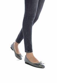 Bailarinas metálicas grises con punta redondeada, pequeño detalle de lazo y un tacón bajo y plano; combinadas con jeans ajustados oscuros.