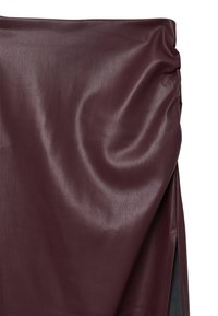 Bordeauxrote Lederrock mit gerafftem Detail an der Seite und einem vorderen Schlitz, der eine glatte, leicht glänzende Textur zeigt.