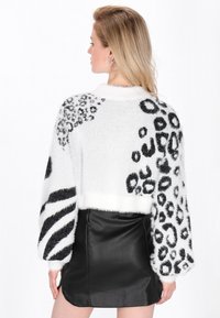 Weißer, flauschiger, kurzer Pullover mit schwarzen Leoparden- und Zebramustern an den Ärmeln, kombiniert mit einem schwarzen Lederrock.
