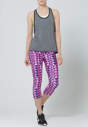 Grå linne med svart kant lagd över en ljusgul topp, ihop med rosa leggings med geometriskt mönster och svarta sportskor.
