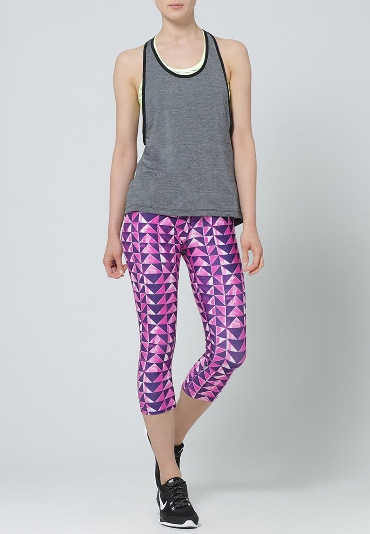 Canottiera grigia con bordi neri sovrapposta a una maglietta gialla chiara, abbinata a leggings rosa con motivo geometrico e scarpe sportive nere.