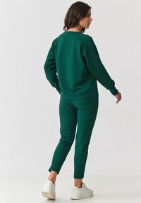 Zielona bluza i dopasowane dresy wykonane z miękkiego materiału, z długimi rękawami, okrągłym dekoltem i luźnym krojem. Białe trampki.