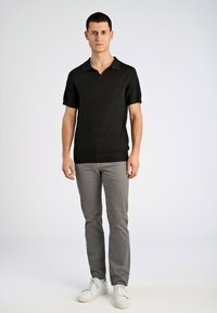 Svart kortärmad pikétröja med krage, texturerad tyg, kombinerad med ljusgrå slim-fit byxor och vita sneakers. Enkelt design, inga mönster.