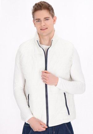 Weiße gesteppte Weste mit hohem Kragen, marineblauem Reißverschluss und seitlichen Taschen. Über einem weißen Langarmshirt getragen, auf einem neutralen Hintergrund präsentiert.