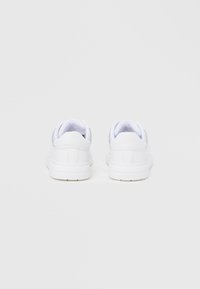 Ζευγάρι λευκά παπούτσια τύπου low-top με λείο δέρμα, σε προβολή από πίσω, σε απλό γκρι φόντο.