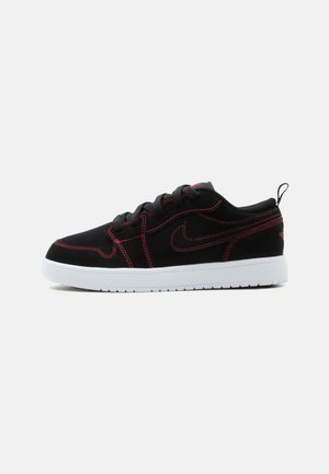 Czarny niski sneaker z czerwonym przeszyciem, logo Nike po boku, czarne sznurowadła i biała podeszwa na jednolitym jasnoszarym tle.