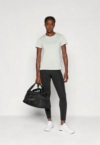 Helehall sportlik T-särk, mustad retuusid ja valged vabaajajalatsid; hoiab käes musta spordikoti valgete detailidega.