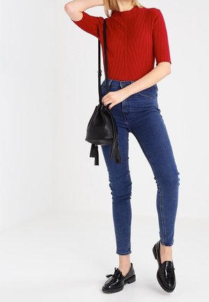 Rød ribbet kortærmet top, high-waisted mørkeblå skinny jeans, sort bucket bag med frynser og sorte loafers med sløjfedetalje.