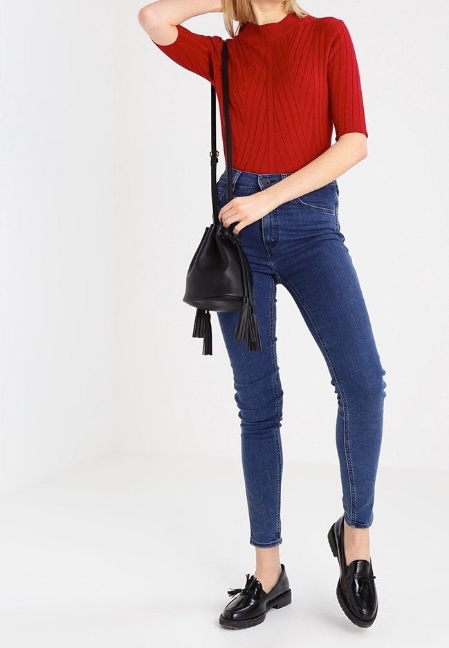 Top corto a maniche corte rosso a coste, jeans skinny blu scuro a vita alta, borsa a secchiello nera con frange e mocassini neri con dettaglio a fiocco.