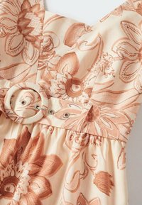 Robe beige avec de grandes impressions florales dans des tons marron et une ceinture assortie avec une boucle ronde recouverte de tissu.