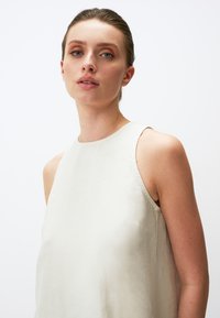 Ärmelloses Top aus Leinen in sanftem Beige mit lockerer Passform, runder Halslinie und minimalen Nähdetails. Sanfte Textur und einfaches Design.