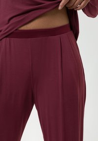 Bordeaux plooibroek van zacht materiaal met een soepele tailleband, voorzien van een relaxte pasvorm en subtiele textuur.