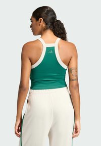 Zelený športový tílko s bielym lemovaním a logom na zadnej strane; kombinované s krémovými teplákmi s zelenými bočnými pruhmi.