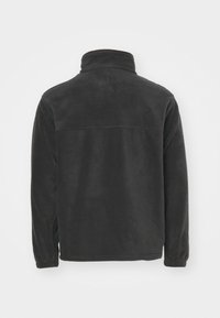 Musth fleece-jakk musta, kõrge kraega, elastsetest mansettidega ja horisontaalse õmblusega seljaosas. Pehme tekstuur ja kerge disain.