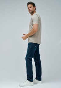 Krémové bavlněné tričko s krátkým rukávem, spárované s tmavě modrými denimovými džíny. Model má na sobě bílé tenisky. Jednoduchý design, uvolněný střih.