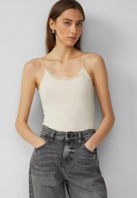 Romantisch crèmekleurig topje met kantafwerking, spaghettibandjes, gecombineerd met hoog gesloten grijze jeans. Zachte textuur, aansluitend ontwerp, minimalistische stijl.