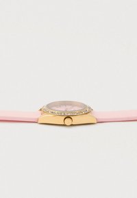 Armbanduhr in Goldtönung mit pinkfarbenem Silikonarmband, pinkem Zifferblatt und rhininsteinbesetzter Lünette, seitlich gezeigt mit sichtbarer Krone.