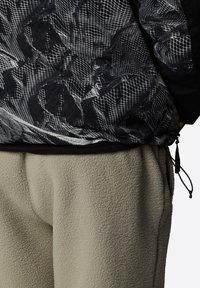 Svart och vit mönstrad hoodie med en texturerad, nätliknande design och cinchad nederdel, tillsammans med ljusbeiga fleecebyxor.