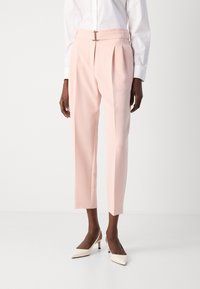 Pantaloni su misura rosa pallido con pieghe, dotati di un dettaglio in argento sulla vita, abbinati a décolleté bianche sporche a punta.