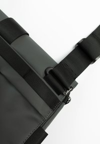 Borsa a messaggero grigia con superficie testurizzata, cinturini neri e chiusura a clip. Presenta una cerniera liscia lungo un bordo.