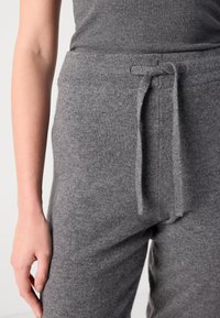 Grå, myk strikkede joggebukser har elastisk midjebånd med snøring. Teksturen er fin, med subtile flekker i stoffet.