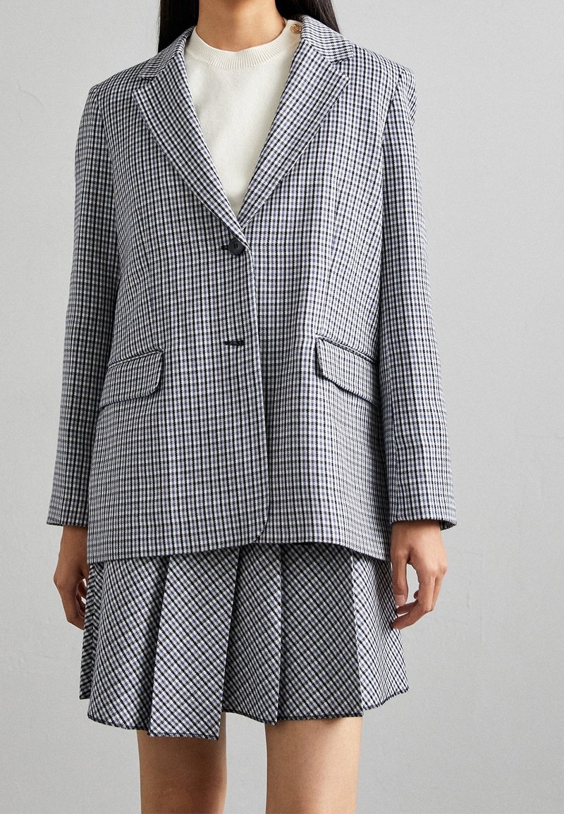 Blazer a cuadros y falda plisada en blanco y negro. El blazer tiene un cuello con muesca y dos bolsillos frontales. Tejido texturizado con un ajuste estructurado.