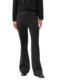 Osoba ubrana w czarne, dopasowane, wysokiego stan, rozszerzane spodnie, zestawione z czarnymi błyszczącymi mokasynami i czarną bluzką z długim rękawem.