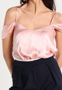Rosa satinblus med avtagna axelärmar. Har en djup urringning och samlad midja. Slät textur mot mörka, skräddarsydda byxor.