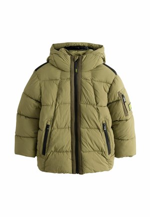 Dreng iført en olivengrøn quiltet dunjakke med hætte, stående med hænderne i lommerne mod en ensfarvet baggrund.
