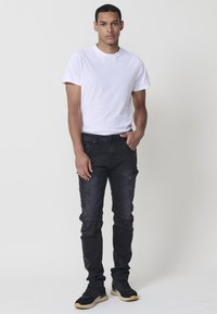 Camiseta blanca de cuello redondo, jeans cargo oscuros con múltiples bolsillos y zapatillas negras con suela texturizada. Diseño simple y ajustado.