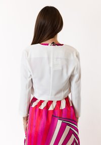 Giacca bianca accorciata con maniche lunghe, abbinata a una gonna con strisce verticali vivaci in rosa e rosso e motivi geometrici.