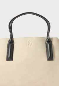 Beige læder tote taske med sorte håndtag, prydet med prægede logoer og kontrasterende syninger. Glat tekstur med struktureret form.