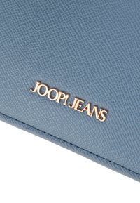 Modrý textúrovaný peňaženka so zlatým nápisom "JOOP! JEANS" na spodnej strane, ktorá má elegantný dizajn a prešité okraje.