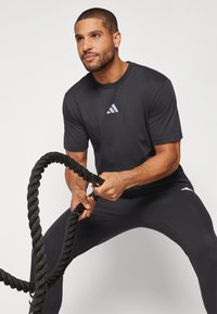 Zwart atletisch T-shirt met korte mouwen en een klein wit Adidas-logo op de borst, gecombineerd met zwarte aansluitende broek en dikke zwarte touwen.