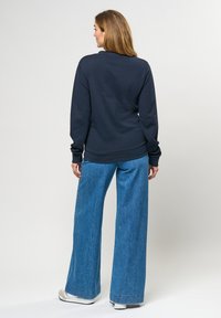 Námořnický svetr s dlouhými rukávy a žebrovanými manžetami, kombinovaný s širokými světle modrými džíny a bílými teniskami. Jednoduchý, uvolněný design.