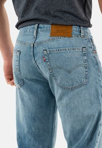 Jeans in denim azzurro chiaro con cuciture a contrasto, due tasche posteriori con il logo Levi's e un'etichetta in pelle marrone sulla cintura.
