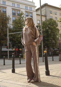 Bruine sweatshirt met een voorknopzak en contrasterende zijstrepen; bijpassende bruine broek; casual schoenen; stedelijke buitenomgeving.
