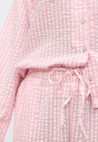 Ελαφρύ σετ πιτζάμας με ροζ και λευκό καρό σχέδιο, με πουκάμισο με κουμπιά και παντελόνι με ελαστική μέση, σε υφή υ φάσματος και λεπτομέρεια φιόγκου.