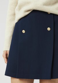 Jupe bleu marine à coupe droite avec une double rangée de boutons dorés sur le devant. Le matériau semble lisse avec une texture subtile.