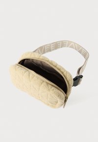 Quiltet beige taske lavet af tekstureret materiale med en kontrasterende mørk indvendig. Har en lynlåslukning og justérbar strop med logo.