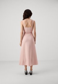 Vestito maxi rosa con spalline sottili, corpino aderente e gonna svasata. Presenta un dettaglio con cintura brandizzata e un tessuto liscio e testurizzato.
