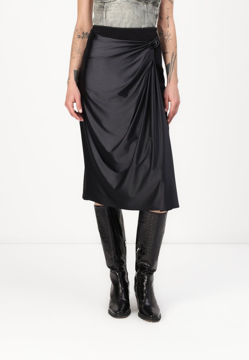 Black draped midi skirt with a smooth texture, featuring a side knot detail and a wide waistband, paired with knee-high glossy black boots.