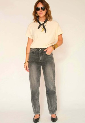 Jean en denim gris taille haute avec un fini délavé, associé à un t-shirt ample crème et des lunettes de soleil noires. Accessoirisé avec une écharpe noire.