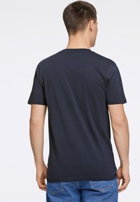 Camiseta de algodón azul marino de manga corta, cuello redondo y textura suave, mostrada desde la parte de atrás. Detalles mínimos y sin patrones.