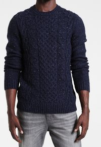 Granatowy sweter z dzianiny z motywem warkocza, z prążkowanymi mankietami i dołem, wykonany z teksturowanej włóczki z delikatnymi kropeczkami.